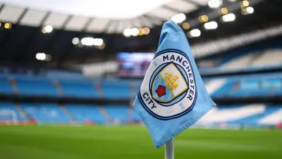 Manchester City club crest outside a stadium, with tax investigation headlines